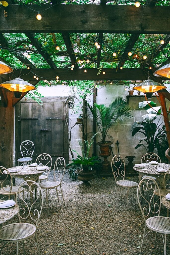 Cafe with setting on ornamental tables near chairs under decorative lamps in backyard on summer day