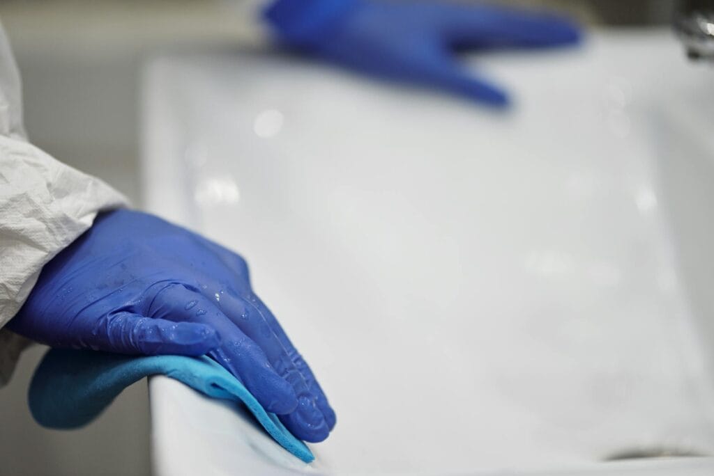 Close-up of a person sanitizing a bathroom sink with gloves and cloth, focusing on hygiene and cleanliness.